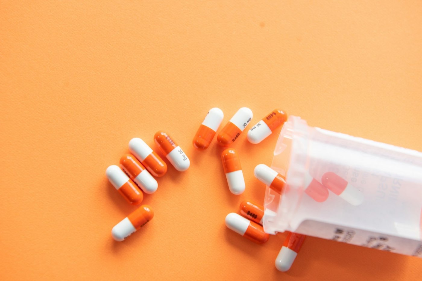 Orange and white capsules spilling from a container onto a plain background